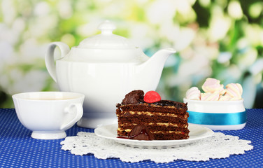 Teapot, cup of tea and delicious cake on natural background