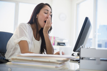 Caucasian businesswoman yawning at desk