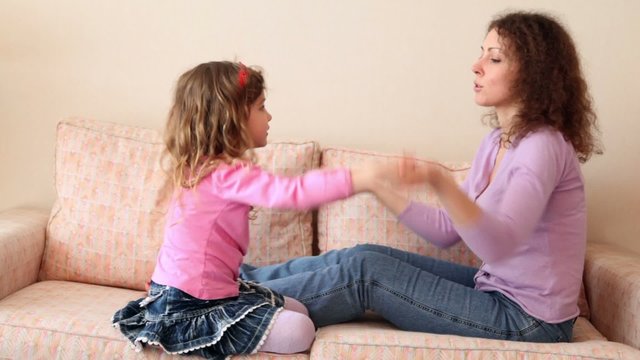 Mother and her little daughter sit on sofa and play hands