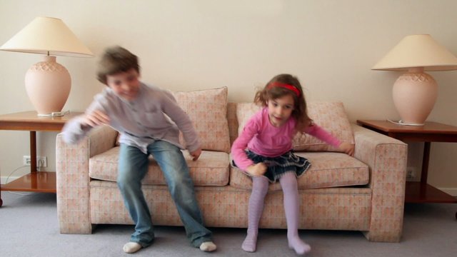 Two kids boy with girl come in room, sit and jump on sofa