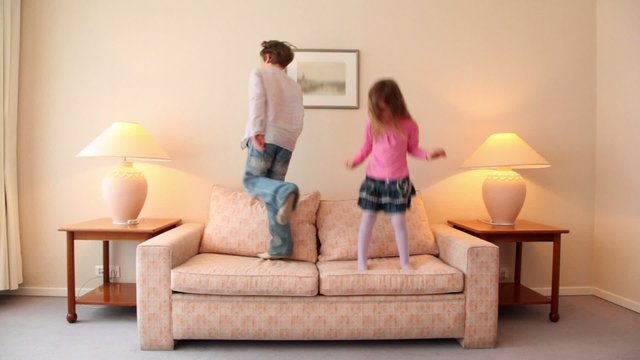Two kids jump on sofa at room with lamps on each side