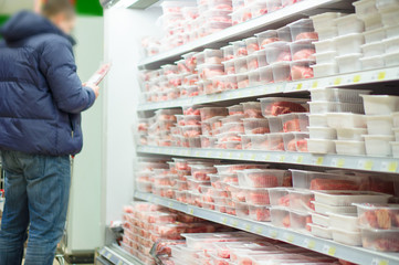 Customer select beef slices in plastic boxes on shelves in super