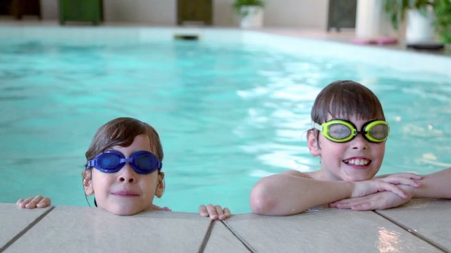 Two kids in swimming glasses stay on pool edge