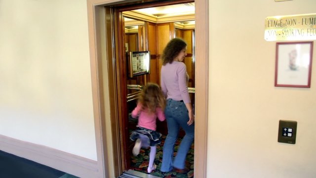Doors opens and mother with daughter walk in elevator