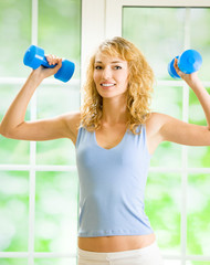 Young smiling woman with dumbbells, indoors