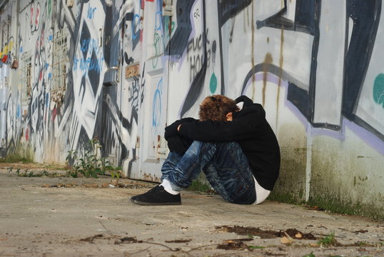 Jugendlicher sitzt traurig vor Grafitti