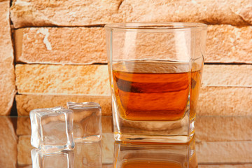 Glass of whiskey and ice on brick wall background