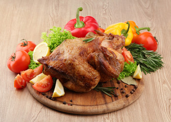 Whole roasted chicken with vegetables on plate, on wooden table