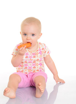 Sweet little baby eating a carrot sitting on the floor on white