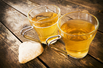 Two cups of tea a plank of wood next to a heart-shaped cake.