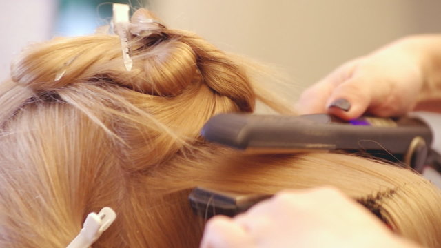 Hairdresser straightens model's hairs using hair iron