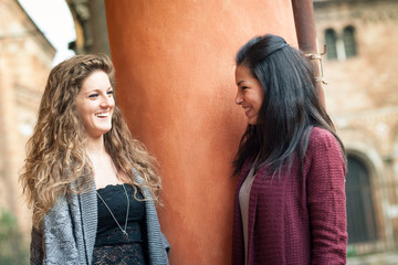 Two girls talking outdoors in S. Stephen square, Bologna, Italy.