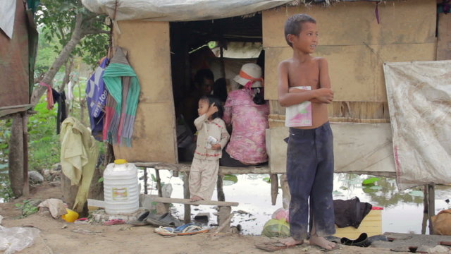 Boy in slum holding book, background his family in shack