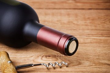 Bottle of wine with corkscrew on wooden background