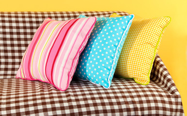 Colorful pillows on couch on yellow background