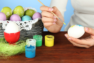 Young woman painting Easter eggs, on color background