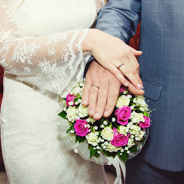 Hands of the bride and groom lying on the bridal bouquet