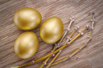 Three gold eggs and spring branch at Easter. On a wooden texture