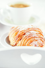 Croissant with coffee, on sunlit breakfast tray