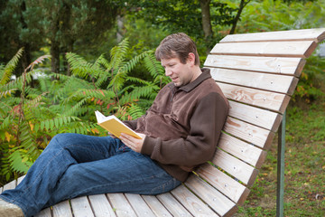 Young man reading book on bench in summer forest