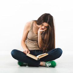 Beautiful young woman sitting on floor with book