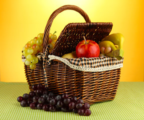 Picnic basket with fruits on cloth on yellow background