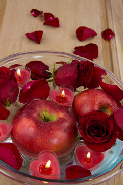 Apple with rose petals and heart candles in glass bowl