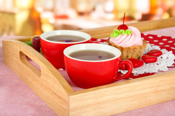 Cups of tea with cake on wooden tray on table in cafe