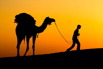 Silhouette of a man and camel at sunset in India