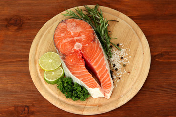 Fresh salmon steak on cutting board, on wooden background