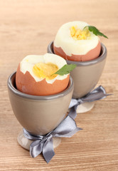 Boiled eggs in egg cups, on wooden table