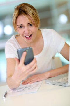 Woman in office looking at smartphone with scary look
