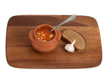 Soup in clay pot with bread and garlic on wooden kitchen board