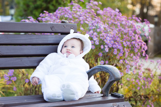 Baby Girl In White Snowsuit On A Bench