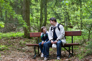 Fototapeta premium Father and son relaxing on bench after hike in the woods