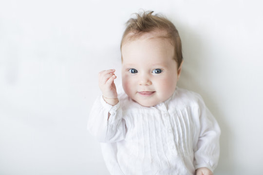 Beautiful baby blue eyes in white dress onwhite blanket
