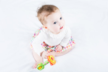 Sweet baby girl playing with a toy sitting on a white blanket