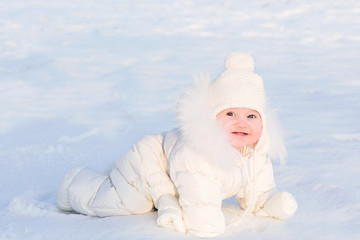 Cute baby in a white fur suit crawling in snow