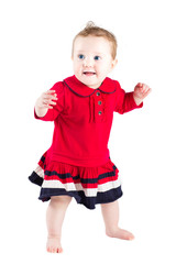 Beautiful baby girl in a red dress making her first steps