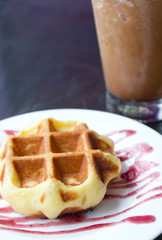 Waffle on plate with iced coffee on background.