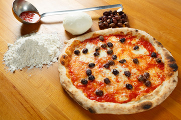 Italian Pizza, ingredients in the background on a wood table