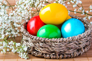 Colored painted eggs in a wattled basket with flowers