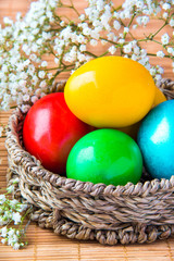 Colored painted eggs in a wattled basket with flowers