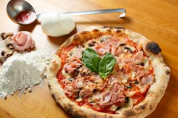 Typical Italian Pizza, ingredients in background on wood table