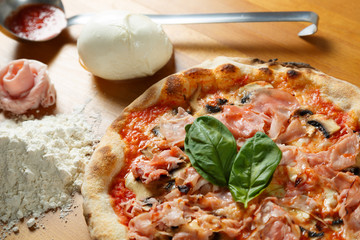 Typical Italian Pizza, ingredients in background on wood table