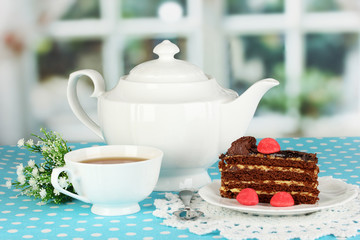 Teapot, cup of tea and delicious cake on window background