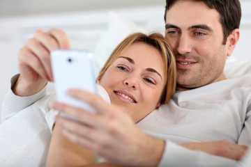 Fototapeta premium Couple laying in sofa and using spartphone