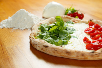 Typical Italian Pizza, ingredients in background on wood table