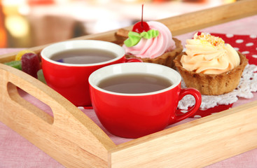 Cups of tea with cakes on wooden tray on table in cafe