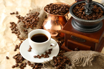 Cup of coffee, pot and grinder on beige background